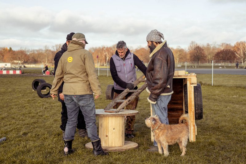 4 Menschen und ein Hund bei der Planung eines Hindernisses aus alten Baumaterialien